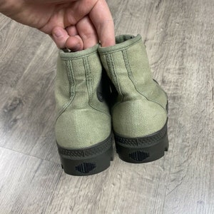 K&ouml;nnte beinhalten: Ein Paar gr&uuml;ne Canvas-High-Top-Sneaker mit schwarzen Gummisohlen und dem Wort "PALLADIUM" auf den Sohlen.