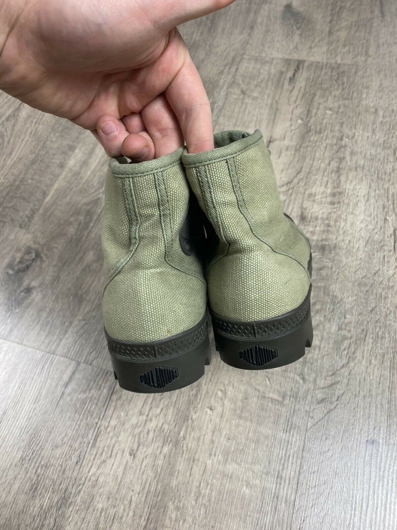 K&ouml;nnte beinhalten: Ein Paar gr&uuml;ne Canvas-High-Top-Sneaker mit schwarzen Gummisohlen und dem Wort "PALLADIUM" auf den Sohlen.