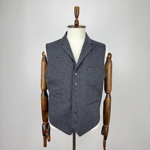 Puede incluir: Un chaleco gris carbón con solapa de muesca y cierre de botones. El chaleco tiene dos bolsillos delanteros y se exhibe en un maniquí de madera. La tela es texturizada.