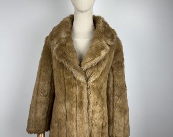 May include: A tan faux fur coat with a classic collar and three-quarter sleeves. The coat is displayed on a mannequin. The fur has a vertical pattern and a soft, textured appearance. A vintage-inspired outerwear piece.