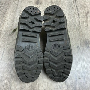 K&ouml;nnte beinhalten: Ein Paar schwarze Gummisohlige Stiefel mit einem Profilmuster. Die Stiefel sind aus hellgr&uuml;nem Canvas-Material gefertigt.