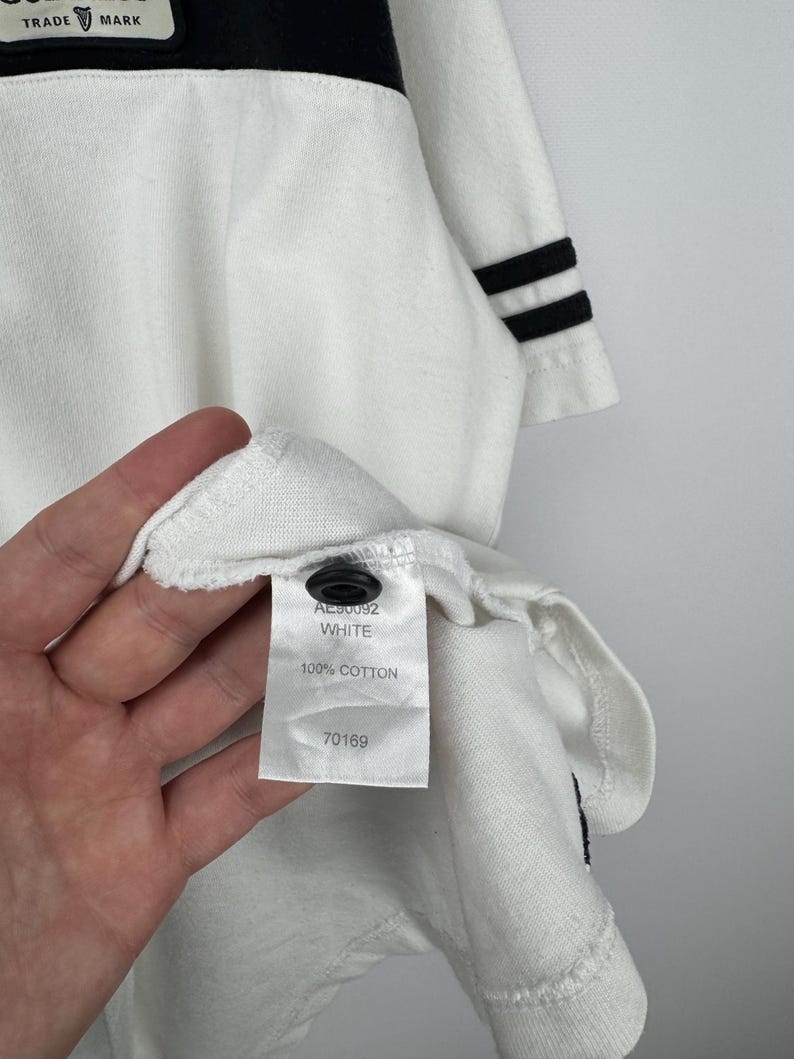 May include: White long-sleeved shirt with a black stripe across the chest and black stripes on the sleeve cuffs. The shirt has a tag that reads "AL90092 WHITE 100% COTTON 70169". The shirt has a black button.