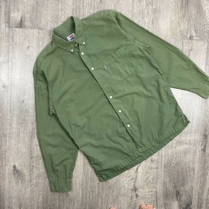 Op de afbeelding: Een lang mouw, groen overhemd met knopen en een borstzak.