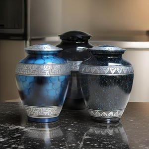 Pode incluir: Tr&ecirc;s urnas decorativas em tons de azul e preto. As urnas t&ecirc;m faixas prateadas com padr&otilde;es de folhas e geom&eacute;tricos. As urnas azuis t&ecirc;m um efeito marmorizado, enquanto a urna preta tem um design salpicado. As urnas s&atilde;o exibidas em uma superf&iacute;cie escura e salpicada.