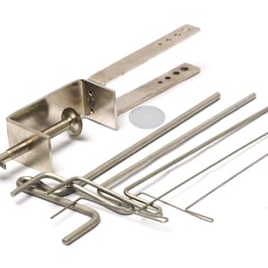 May include: A collection of stainless steel metal tools, including a clamp with a screw mechanism, several straight rods, and bent wire pieces. The tools are arranged on a white surface, suggesting a workshop or industrial setting.
