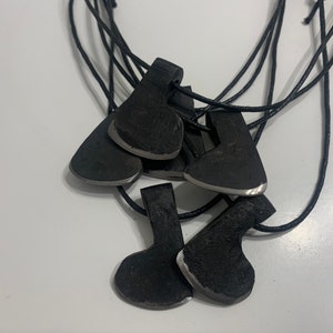 May include: A necklace with five small axe-shaped pendants. The pendants are made of black metal and have a silver-colored edge. The necklace is made of black cord.
