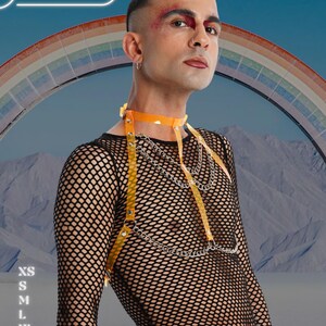May include: A person wearing a black fishnet top with an orange harness and silver chain accents. The harness includes a choker and straps. The background features a rainbow and the text "HARNESSIRE".