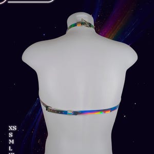 May include: A holographic harness displayed on a white mannequin. The harness has a reflective, iridescent finish with silver-tone hardware. The brand name "HARNESSIRE" is visible in the top left corner. Sizes XS to 2XL are listed on the left side.