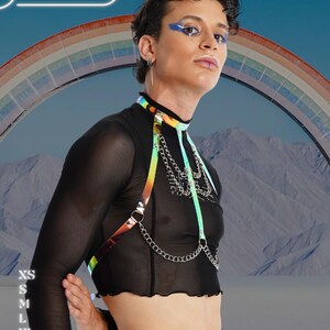 May include: A black mesh top with a rainbow harness and silver chain detail. The image includes the text "HARNESSIRE" and size options: XS, S, M, L, XL, and 2XL. A rainbow and mountain range are in the background.