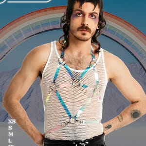 May include: White mesh tank top with a holographic harness featuring silver rings. The image includes the text "HARNESSIRE" and size options: XS, S, M, L, XL, and 2XL. A rainbow is in the background.