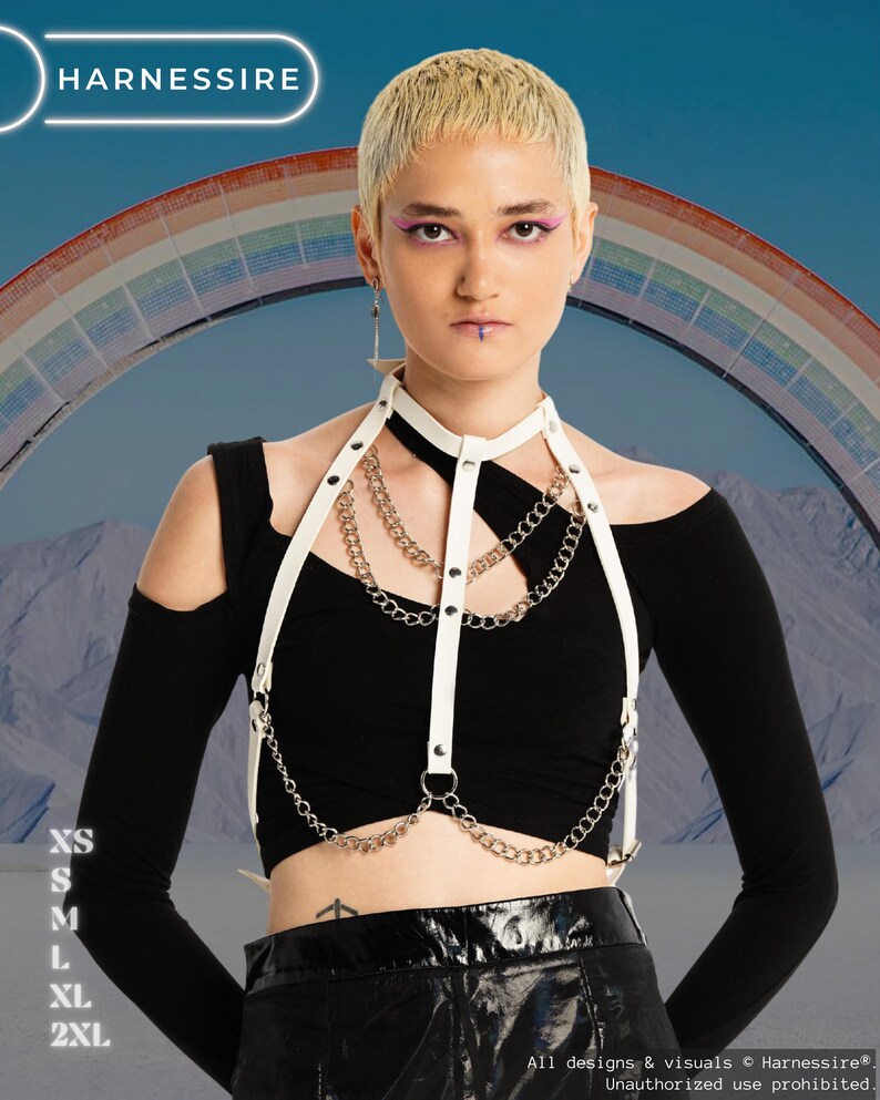 May include: A white leather harness with silver chains and black accents. The harness is worn over a black off-the-shoulder top. The image includes the text "HARNESSIRE" and size options: XS, S, M, L, XL, and 2XL. A rainbow is in the background.
