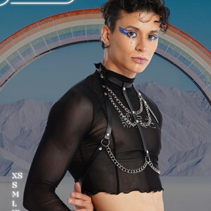 May include: Black mesh long-sleeve top with a leather harness and silver chain detailing. The model is wearing blue eye makeup and a lip piercing. The background features a rainbow and the text "HARNESSIRE". Sizes XS to 2XL are listed.