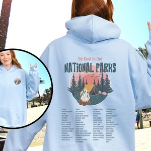 May include: Light blue hooded sweatshirt with a graphic print of a campfire scene in a forest with the text "Be Kind to Our NATIONAL PARKS" and a list of all the national parks in the United States.