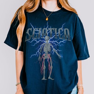 May include: A navy blue t-shirt with a graphic of a skeleton with lightning bolts and the word "Sciatica" printed on the front.