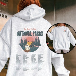 May include: A gray hooded sweatshirt with a graphic print of a campfire scene in a forest. The text "Be Kind to Our National Parks" is printed above the graphic. A list of national parks is printed below the graphic.