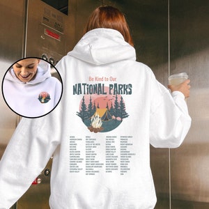 May include: White hooded sweatshirt with a graphic of a campfire in a forest with the text "Be Kind to Our National Parks" and a list of national parks printed on the back.