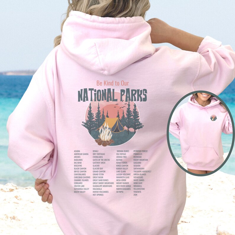 May include: Pink hoodie with a graphic design of a campfire in a forest with the text "Be Kind to Our National Parks" and a list of national parks printed below the graphic.