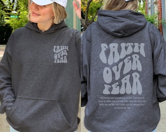 Puede incluir: Sudadera con capucha gris carbón con el texto "Faith Over Fear" en la parte delantera y trasera. La parte trasera de la sudadera con capucha también presenta un versículo bíblico. La sudadera con capucha tiene un bolsillo delantero y una capucha con cordón. El texto es de color gris claro.