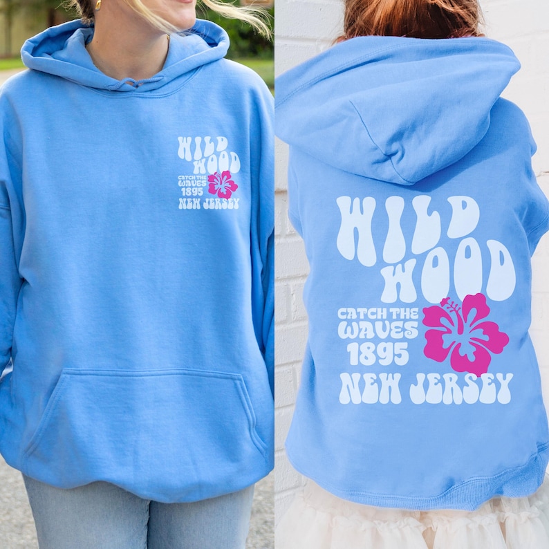 Może przedstawiać: Jasno błękitna bluza z kapturem z napisem "WILDWOOD CATCH THE WAVES 1895 NEW JERSEY" w kolorze białym i grafiką r&oacute;żowego hibiskusa.
