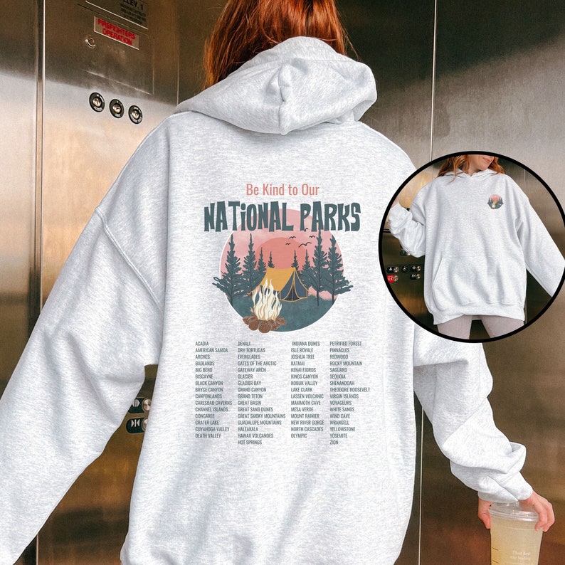 May include: A gray hooded sweatshirt with a graphic print of a campfire scene in a forest. The text "Be Kind to Our National Parks" is printed above the graphic. A list of national parks is printed below the graphic.