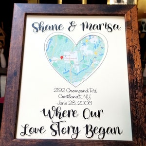 May include: A framed print featuring a map within a heart shape, with the names "Shane & Marisa" above. The print includes the address "2192 Crompond Rd, Cortlandt, NY" and the date "June 28, 2006", with the text "Where Our Love Story Began". The frame is dark brown.