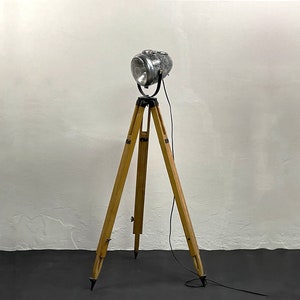 May include: A vintage silver spotlight on a wooden tripod stand. The spotlight has a round reflector and a black cord.