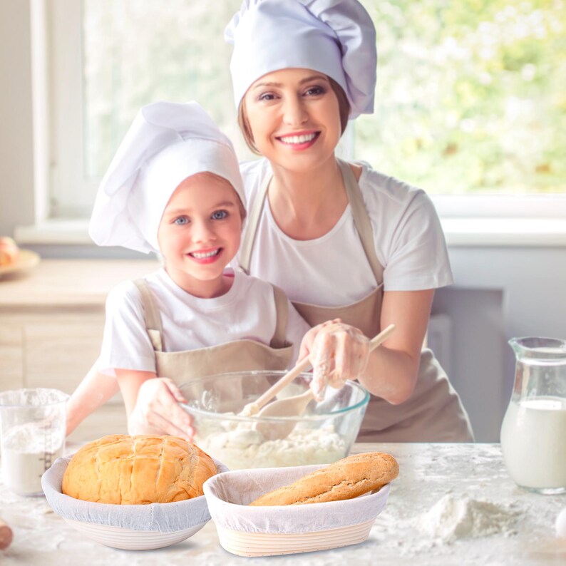 May include: Two people wearing white chef hats are baking bread. A round loaf of bread is in a white proofing basket and a long loaf of bread is in a rectangular proofing basket.