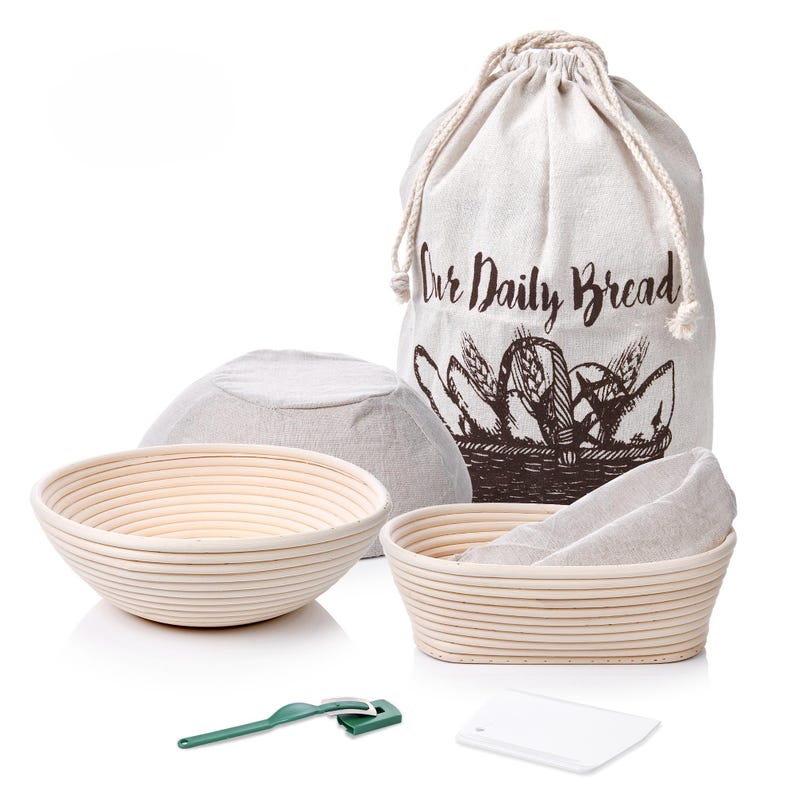 May include: A set of three bread proofing baskets, two round and one oval, with linen liners. The set also includes a green dough scraper and a white plastic dough lame. The baskets are in a white canvas bag with the text "Our Daily Bread" printed on it.