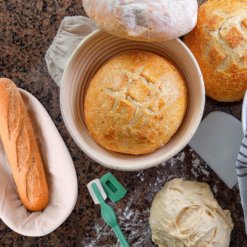 May include: A close-up of three loaves of bread, one in a white ceramic bowl, one on a white surface, and one on a wooden surface. The bread is golden brown and has a crusty exterior.