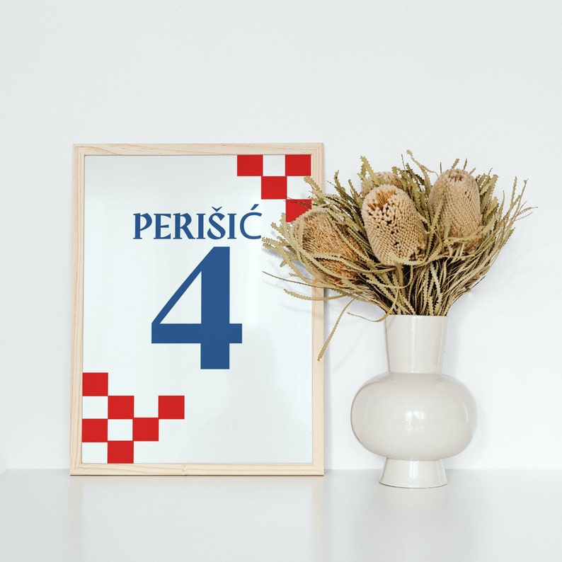 Puede incluir: Una impresi&oacute;n enmarcada con un patr&oacute;n de cuadros rojos y blancos y el texto "PERI&Scaron;IĆ 4" en azul. El marco es de madera clara y est&aacute; sobre una superficie blanca. Un ramo de flores secas en un jarr&oacute;n blanco est&aacute; a la derecha del marco.