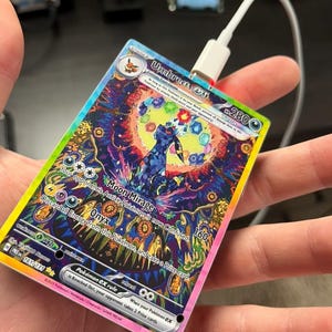 Può includere: Una carta da gioco di scambio Pokemon olografica con Umbreon EX. La carta ha uno sfondo arcobaleno con un Umbreon nero e blu al centro. Il testo della carta recita "Umbreon EX" e "Moon Mirage".