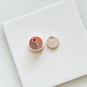 May include: A close-up of a round, pink silicone mold with a geometric pattern. The mold is next to a white, round, geometric patterned pendant.