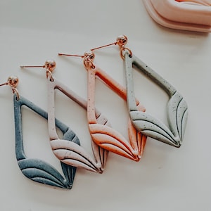 Könnte beinhalten: Drei Paar Hängeohrringe mit einer geometrischen Diamantform. Die Ohrringe sind aus Polymer Clay gefertigt und haben eine gesprenkelte Oberfläche. Die Farben sind ein helles Grün, ein helles Rosa und ein helles Orange.