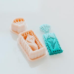 Op de afbeelding: Een set van drie keramische mokken met een gespikkelde, matte afwerking. Elke mok heeft een andere kleur: lichtblauw, crème en grijs. De mokken hebben een eenvoudig, modern ontwerp met een afgeronde vorm en een oor.