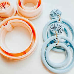 May include: A selection of polymer clay tools and earrings. The tools are in peach hues and include circle cutters. The earrings are light blue with gold hoops and seashell-shaped details.
