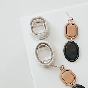 May include: Two pairs of earrings with geometric shapes. One pair is black and brown, the other is tan and black. The earrings are made of polymer clay and have a gold-tone finish.