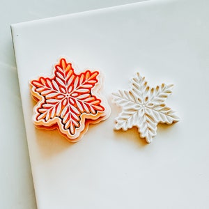 以下が含まれることがあります： 白い表面に、赤い雪の結晶と白い雪の結晶の2つのクッキー型