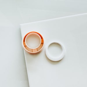 May include: Two round plastic lids, one with a raised orange rim and the other white. The lids are on a white surface.