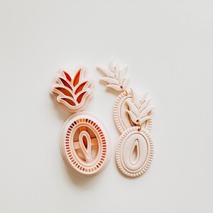 May include: Four light pink polymer clay cutters for crafting. The cutters include two leaf-shaped designs, and two oval-shaped designs with interior cutouts. The cutters are arranged on a white surface.