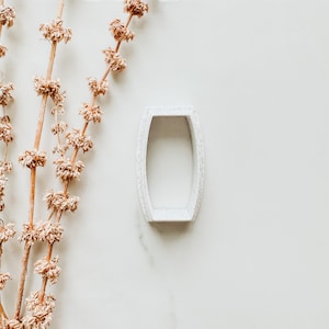 Può includere: Piatto porta anelli in ceramica bianca di forma rettangolare con un bordo leggermente rialzato. Il piatto è su una superficie di marmo bianco.