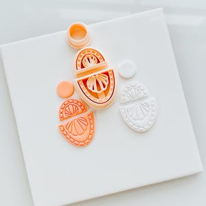 Puede incluir: Un juego de tres moldes de silicona para hacer pendientes de resina. Los moldes tienen forma de concha y son de color melocotón y blanco.