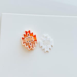 May include: Two cookie cutters, one orange and one white, shaped like a geometric design with a central circle.