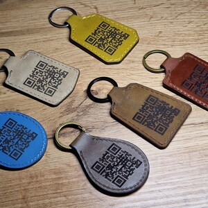 May include: Six leather keychains with different colored leather and a black QR code design. The keychains are on a wooden surface.