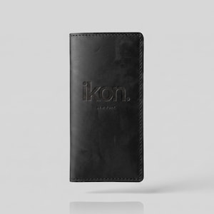 May include: A black leather wallet with the embossed text "ikon. NEW YORK". The wallet is rectangular and appears to be closed. The edges are stitched with a contrasting thread. The wallet is shown against a light gray background.