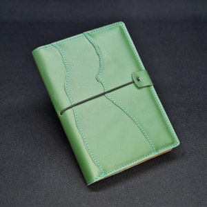 Puede incluir: Un diario de cuero verde con un patrón de puntadas decorativas y un cierre elástico negro.