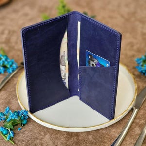 May include: A blue leather wallet with a card slot and a billfold. The wallet is open and has a credit card and cash inside.