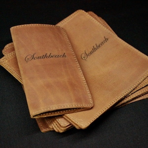 Könnte beinhalten: Ein Stapel brauner Ledergeldbörsen mit dem Wort "Southbeach" geprägt auf der Vorderseite.