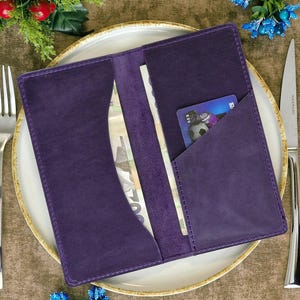 May include: A purple leather wallet with two compartments, one for cash and one for cards. The wallet is lying on a white plate with a blue and green floral design.