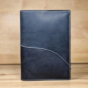 May include: A black leather notebook with white stitching. The notebook has a curved design on the front cover.