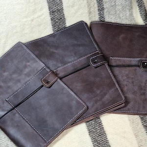 May include: Three brown leather journals with stitched edges and a strap closure. The journals are arranged in a row, with the largest journal at the back and the smallest journal at the front.